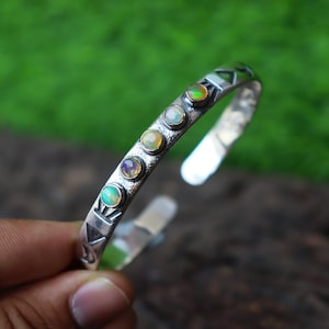 May include: Silver bracelet with five iridescent opal stones set in a row. The bracelet has a textured surface and a simple design.