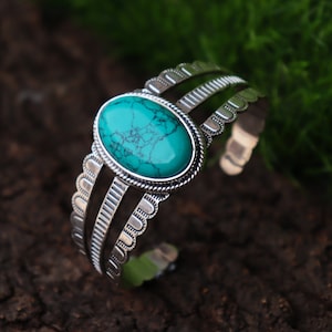 Peut inclure: Un bracelet manchette en argent avec une pierre turquoise sertie au centre. Le bracelet présente un motif décoratif avec trois rangées de bords festonnés.