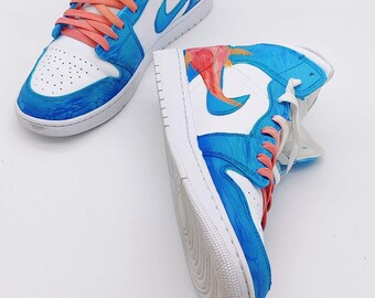 May include: A pair of white high-top sneakers with blue and orange painted designs. The sneakers have white laces and a white sole.