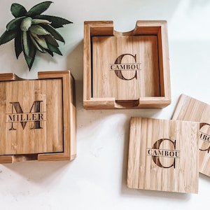 May include: Set of four bamboo coasters with personalized engraved initials and names. The coasters are in a wooden holder. The names are "Miller" and "Cambou".