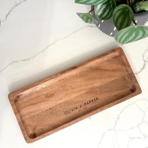 May include: A rectangular wooden serving tray with rounded edges. The tray is made of light brown wood and features the engraved text "OLIVIA & PARKER EST. 2026" in the lower right corner. The tray is empty.