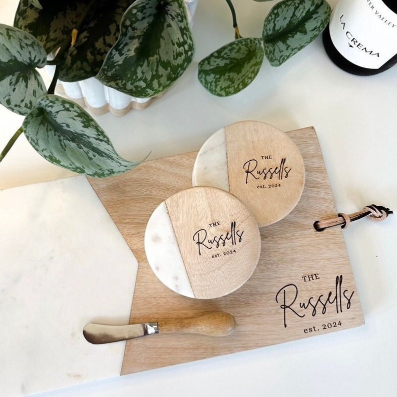 Puede incluir: Una tabla de servir de madera con una incrustaci&oacute;n de m&aacute;rmol y tres posavasos redondos de madera con incrustaciones de m&aacute;rmol. Los posavasos y la tabla de servir est&aacute;n grabados con el texto "The Russells est. 2024".