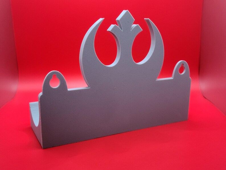 May include: A gray wall shelf with a Rebel Alliance symbol cut out. The shelf has two small holes on the sides.