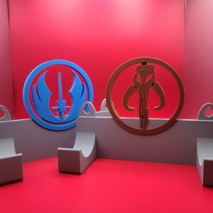 Puede incluir: Dos ganchos de pared con un s&iacute;mbolo azul y un s&iacute;mbolo marr&oacute;n. El s&iacute;mbolo azul es el s&iacute;mbolo de la Alianza Rebelde de Star Wars. El s&iacute;mbolo marr&oacute;n es el s&iacute;mbolo mandaloriano de Star Wars.