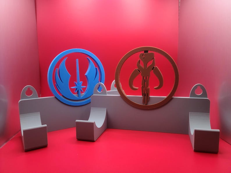 Puede incluir: Dos ganchos de pared con un s&iacute;mbolo azul y un s&iacute;mbolo marr&oacute;n. El s&iacute;mbolo azul es el s&iacute;mbolo de la Alianza Rebelde de Star Wars. El s&iacute;mbolo marr&oacute;n es el s&iacute;mbolo mandaloriano de Star Wars.