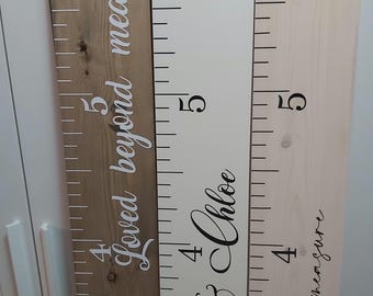 May include: Two wooden growth charts with white and black numbers and text. The left chart is brown wood with white text that reads "Loved beyond measure". The right chart is white wood with black text that reads "Sandra & Chloe" and "Loved beyond measure".