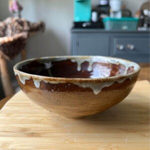 May include: A brown ceramic bowl with a white glaze around the rim. The bowl has a rustic, handmade look.