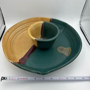 May include: A green and yellow ceramic serving dish with a smaller bowl in the center. The dish has a unique, hand-painted design with swirls and a red accent.