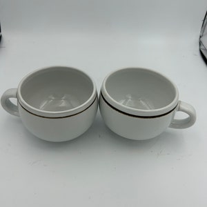 May include: Two white ceramic mugs with a brown stripe around the top.