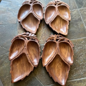 May include: Four wooden leaf-shaped serving dishes. Each dish is carved from a light brown wood and features three compartments. The leaf design includes detailed veining and a decorative stem.
