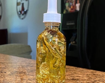 May include: A clear glass bottle with a white dropper top filled with a yellow liquid and gold flakes.