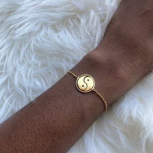May include: A gold chain bracelet with a yin yang symbol charm.