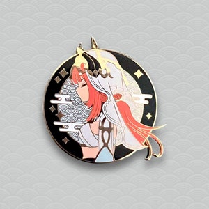May include: A black and gold enamel pin featuring a stylized illustration of a woman with red hair wearing a white veil and a crown. The background is a black circle with gold accents and a wave pattern.