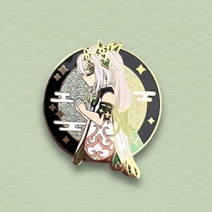 May include: A gold and green enamel pin featuring a character with long white hair, wearing a green and white outfit with a crown. The character is standing in front of a black and gold circle with a moon and clouds design.