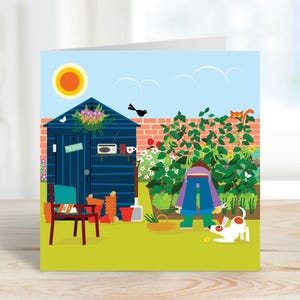 May include: A vibrant greeting card depicting a garden scene. A blue shed with a sign reading "The Office" is visible. A person is gardening, and a dog plays with a ball. A cat is perched on a brick wall, with a sunny sky above.