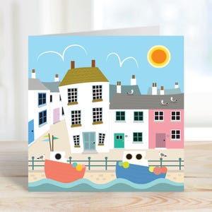 May include: A greeting card featuring a seaside town illustration. The artwork depicts colorful houses, boats, seagulls, and a bright sun against a blue sky. The card has a white border and is suitable for various occasions.