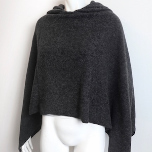 K&ouml;nnte beinhalten: Ein anthrazitfarbener Kapuzenponcho aus weichem Strickstoff. Der Poncho ist &uuml;ber eine wei&szlig;e Schaufensterpuppe gelegt.