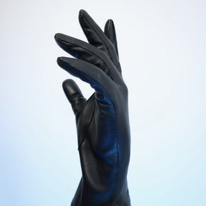 Puede incluir: Un guante de cuero negro, con costuras visibles, se muestra sobre un fondo blanco. El guante es liso y parece estar hecho de cuero de alta calidad. Los dedos est&aacute;n ligeramente curvados, lo que sugiere un ajuste natural. La est&eacute;tica general es elegante.