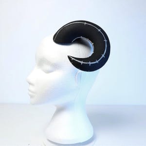 May include: A black foam horn headband with white stitching. The horn is curved and has a pointed tip.