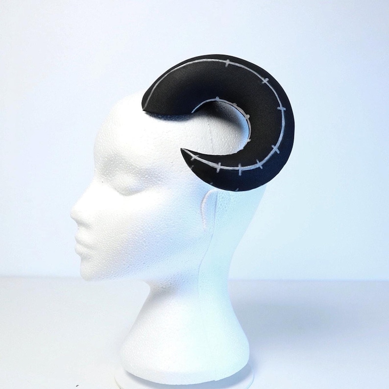 May include: A black foam horn headband with white stitching. The horn is curved and has a pointed tip.