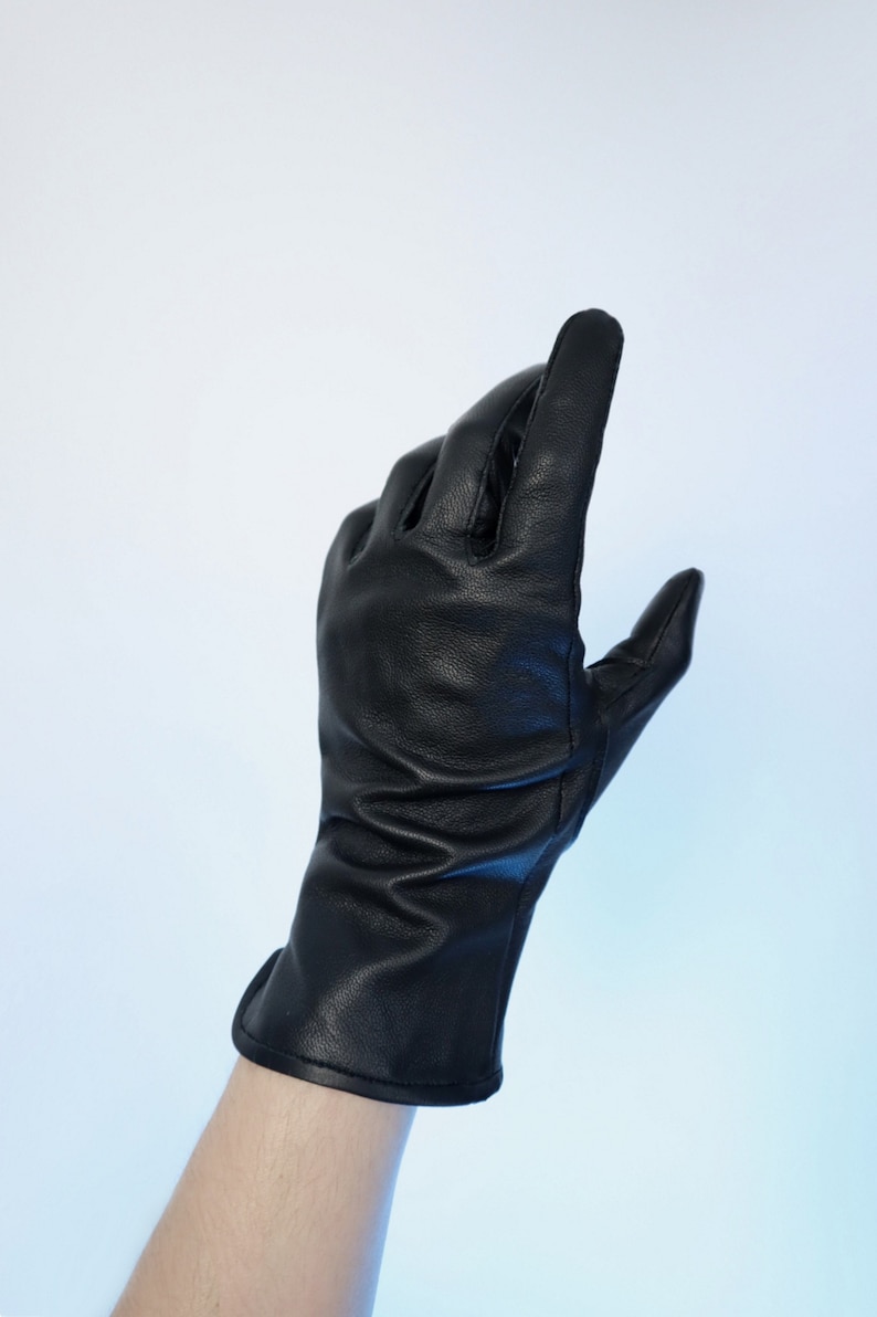 Puede incluir: Un guante de cuero negro con un pu&ntilde;o largo, mostrado sobre un fondo degradado blanco y azul. El guante est&aacute; hecho de cuero liso y tiene costuras visibles. Los dedos est&aacute;n ligeramente curvados, sugiriendo una mano en el interior.