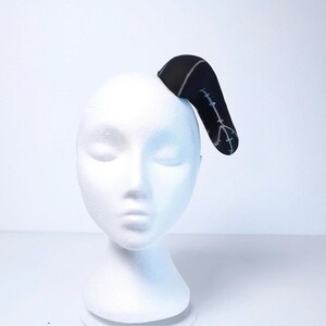 May include: A black headband with a white design of a peace sign and a line of barbed wire. The headband is on a white mannequin head.
