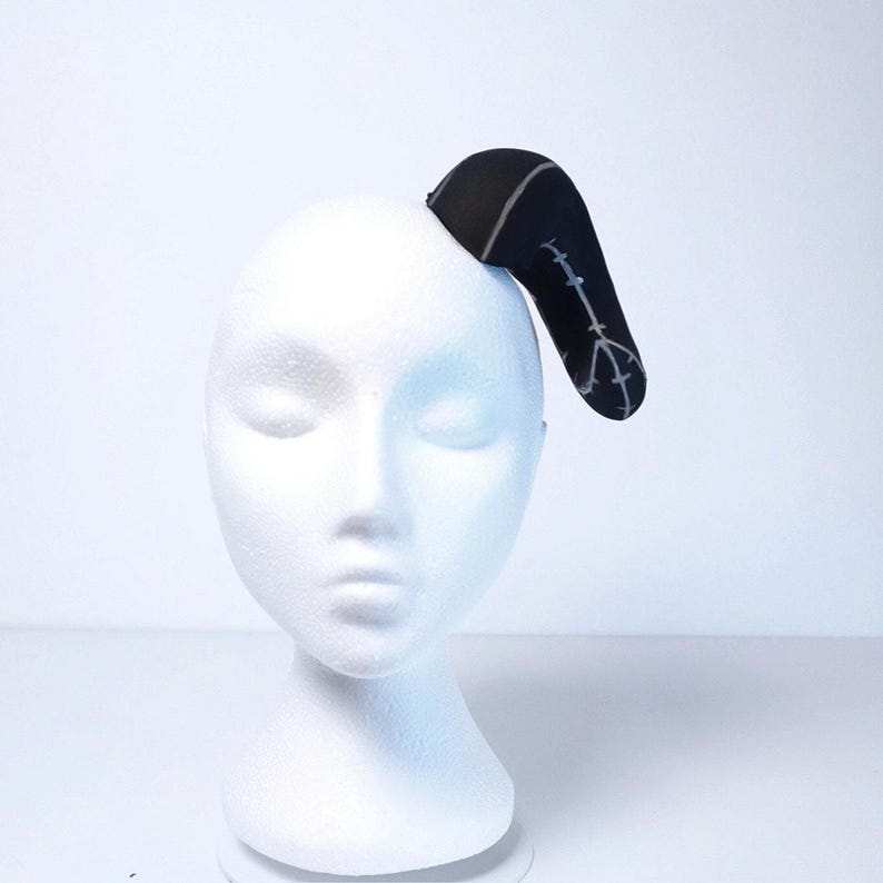 May include: A black headband with a white design of a peace sign and a line of barbed wire. The headband is on a white mannequin head.