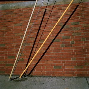 May include: Three yellow poles are leaning against a brick wall. The poles are attached to wires that run across the top of the wall. The wall is made of red bricks.
