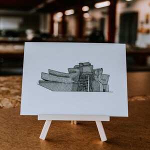 May include: A black and white line drawing of a modern art museum building on a white card mounted on a small wooden easel.