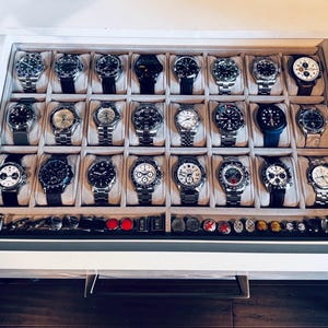 May include: A collection of wristwatches displayed in a white drawer. The watches have various band styles, including stainless steel and leather. The drawer also contains cuff links and watch accessories.