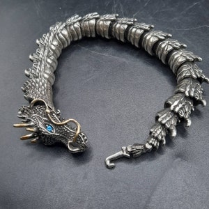 May include: A silver dragon bracelet with a blue gemstone eye. The bracelet is made of interlocking scales and has a clasp.