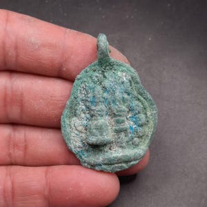 May include: A green metal pendant with a detailed design. The pendant has a loop at the top for attaching to a chain or cord.