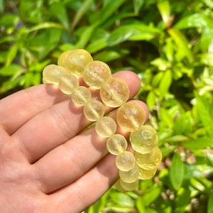 Puede incluir: Un brazalete hecho de cuentas amarillas translúcidas con una superficie texturizada. Las cuentas son redondas y tienen una forma ligeramente irregular.