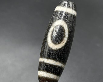 May include: A black and white agate bead with a circular pattern. The bead is oval shaped and has a smooth, polished surface.