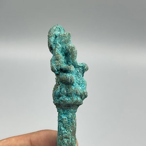 May include: A small, turquoise-coloured, bronze statue of a seated figure. The statue is detailed and has a worn, aged appearance.