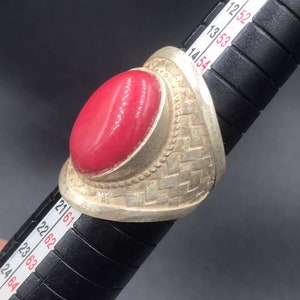 May include: A silver ring with a large, oval-shaped, bright pink gemstone. The ring has a textured, woven design on the band.