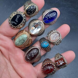 May include: A collection of ten silver rings with various colored stones and engravings. The stones include turquoise, red, green, clear, and blue. Some of the rings have Arabic script engravings.