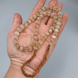 May include: A long strand of light brown, translucent beads with a textured surface. The beads are strung on a brown cord.
