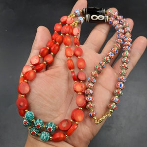 May include: A multi-strand necklace with red coral beads and a strand of colorful, patterned glass beads. The necklace features a black and white agate pendant with an infinity symbol.