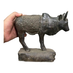 Könnte beinhalten: Eine dunkelbraune Bronzestatue eines Bullen mit aufwendigen Details auf seinem Rücken. Der Bulle steht auf einem rauen, dunkelbraunen Sockel.