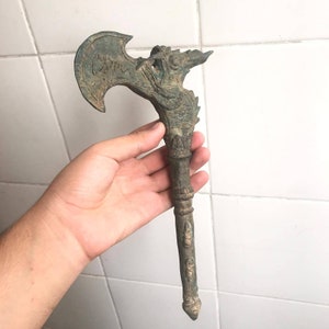 May include: A bronze axe with a dragon head handle. The axe head is decorated with intricate carvings. The handle is detailed with raised designs.