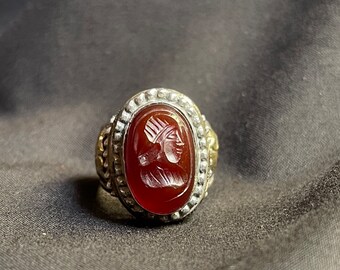 Könnte beinhalten: Ein silberner Ring mit einem roten Karneol-Stein, der ein geschnitztes Design aufweist. Der Stein ist in einer silbernen Fassung mit einem dekorativen Rand gefasst.
