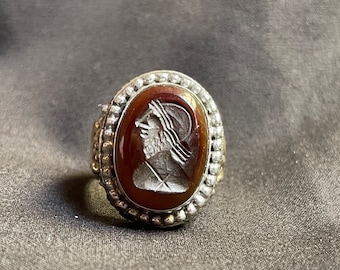 Könnte beinhalten: Ein silberner Ring mit einem braunen ovalen Kamee, der ein geschnitztes Profil einer Person mit Helm zeigt. Der Kamee ist von einem Rand aus kleinen silbernen Perlen umgeben.