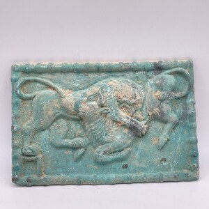 Könnte beinhalten: Eine rechteckige Bronzeplatte mit einem Reliefdesign eines Löwen, der einen Stier angreift. Die Platte hat eine grüne Patina und ist von einem dekorativen Rand umgeben.