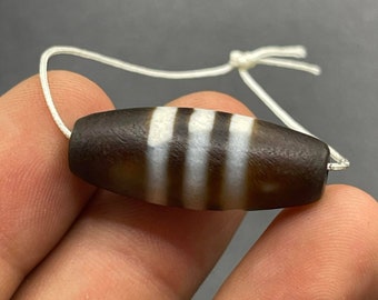 May include: A brown and white agate bead with four white stripes. The bead is strung on a white cord.