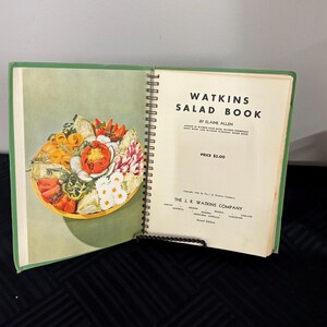 May include: A green and white cookbook titled "Watkins Salad Book" by Elaine Allen. The book is open to a page with a colorful salad in a bowl. The price is $2.00.