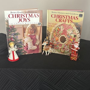 May include: Two vintage Christmas craft books from Better Homes and Gardens. The book on the left is titled "Christmas Joys" and features a young girl in a red dress holding a Christmas stocking. The book on the right is titled "Christmas Crafts" and features a wreath with a red bow and a Santa Claus figure.