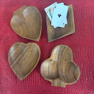 May include: Four wooden serving dishes in the shapes of a heart, a club, and a square, with playing cards in one. The dishes are made of a warm-toned wood and sit on a red textured surface. The playing cards are the Ace of Clubs, and the 10 of Hearts and Diamonds.