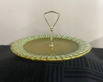 May include: A green ceramic serving tray with a gold metal handle. The tray has a scalloped edge and a raised center.