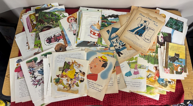 May include: A collection of vintage children's book pages, featuring colorful illustrations and text. The pages depict various scenes, including a fire truck, a doll, and a king. The pages are stacked on a wooden surface.